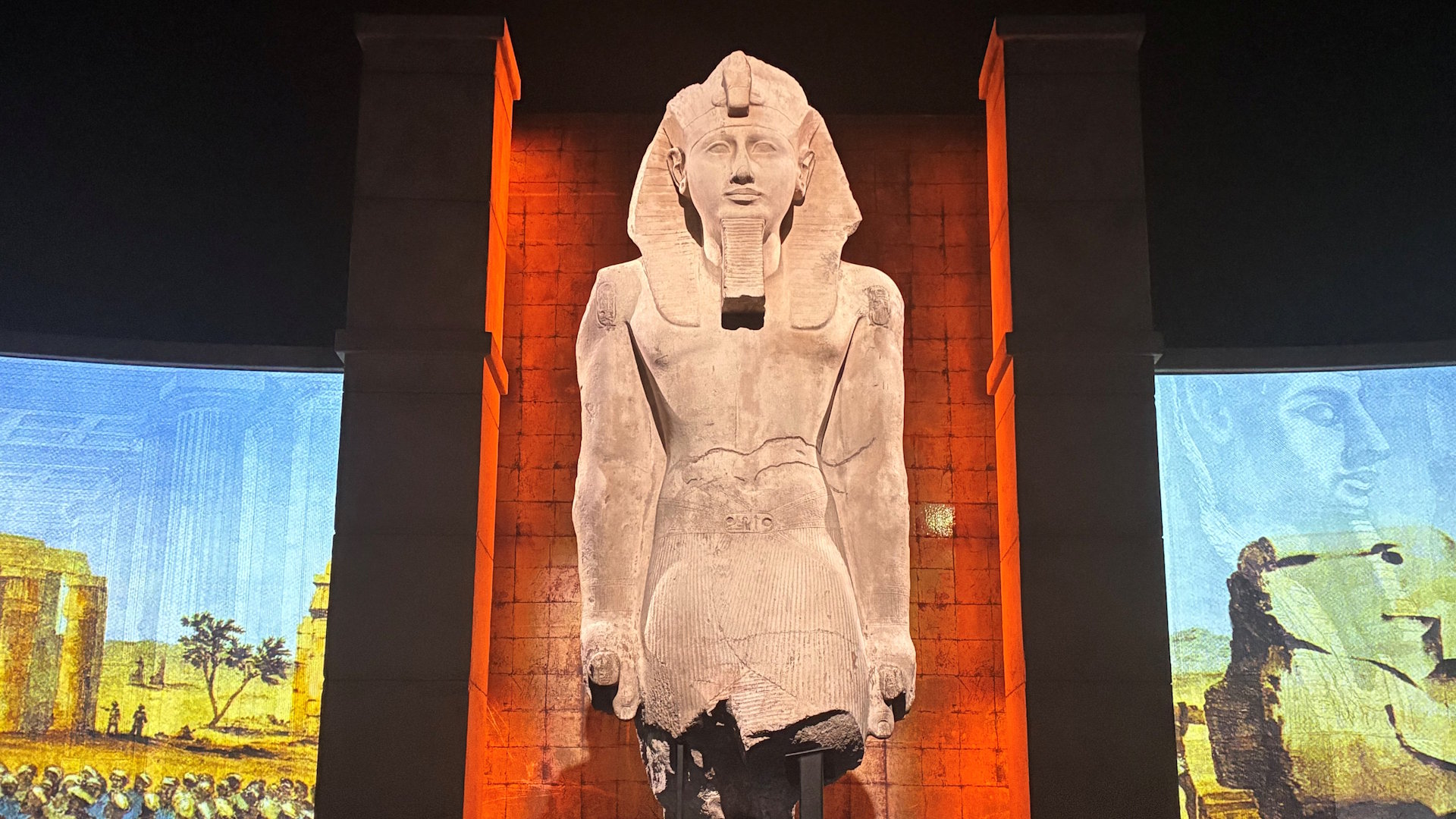 A statue of Ramses II showing his headdress and torso, illuminated from the front.