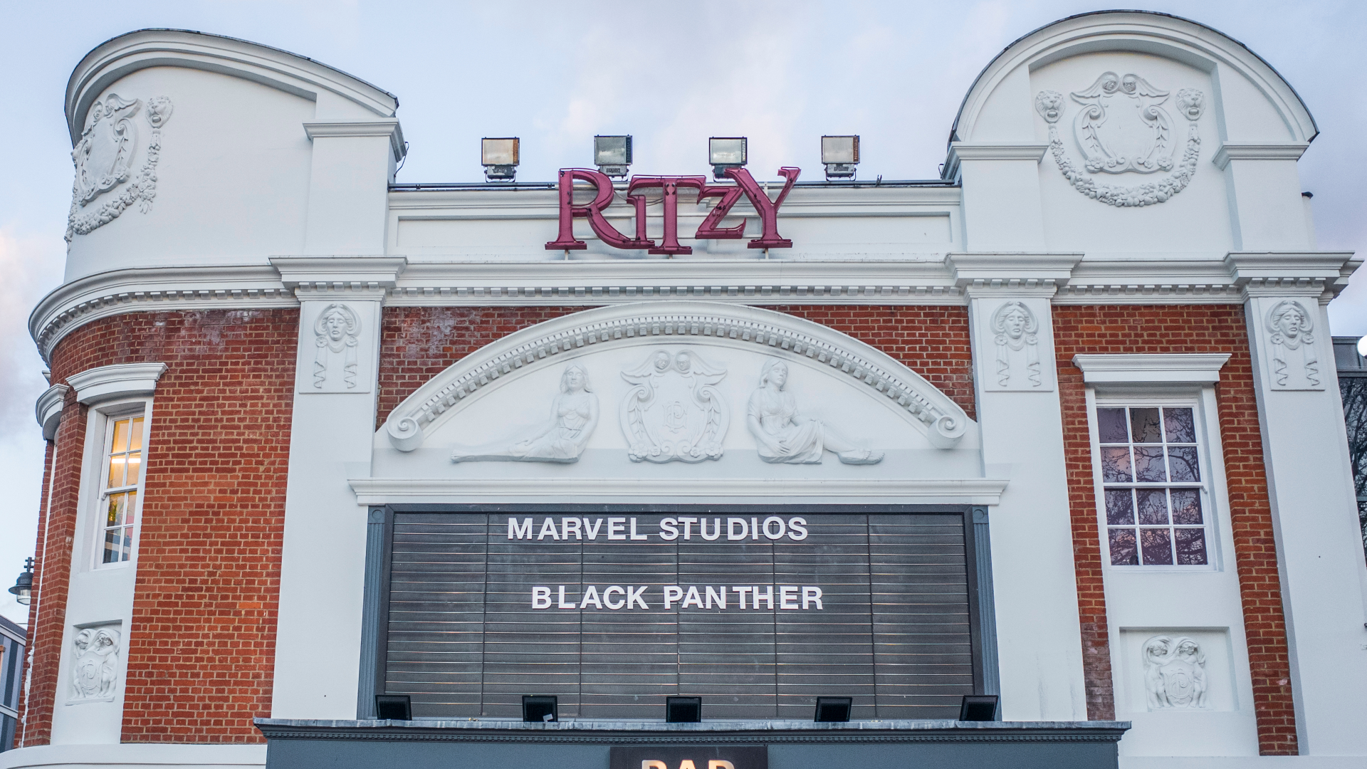 A photo of the front exterior of Ritzy Cinema with its original proscenium arch, a black board spelling out the name of the films on show and red Ritzy lettering