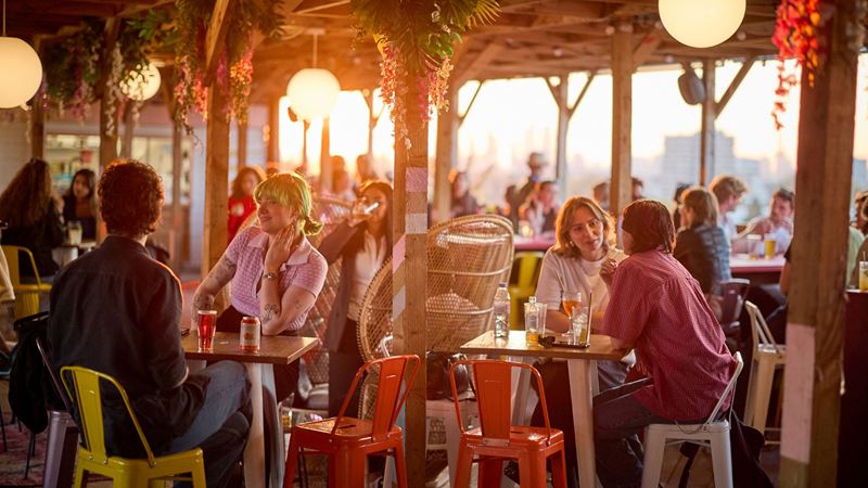 People sit in the sunset glow on a rooftop bar in London.
