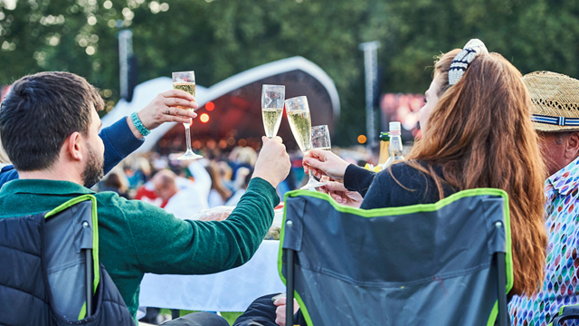 A family cheers with glasses of champagne sat on camping chairs in front of the stage at Battersea Park in Concert