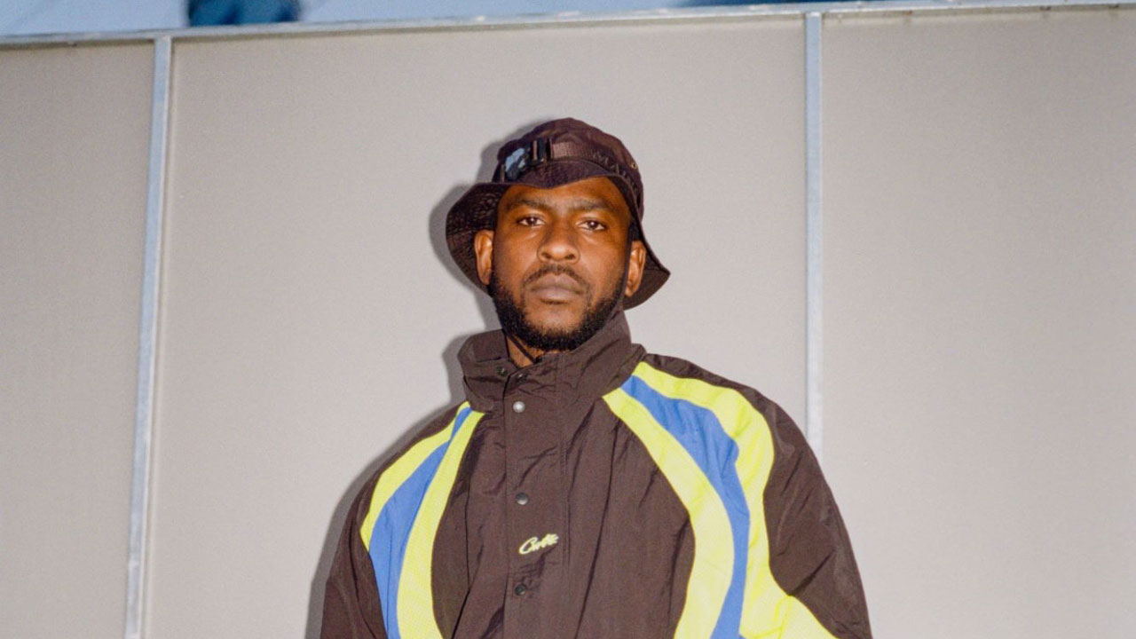 A photo of Skepta backstage at Big Smoke Festival wearing a bucket hat and Corteiz tracksuit taken on a film camera
