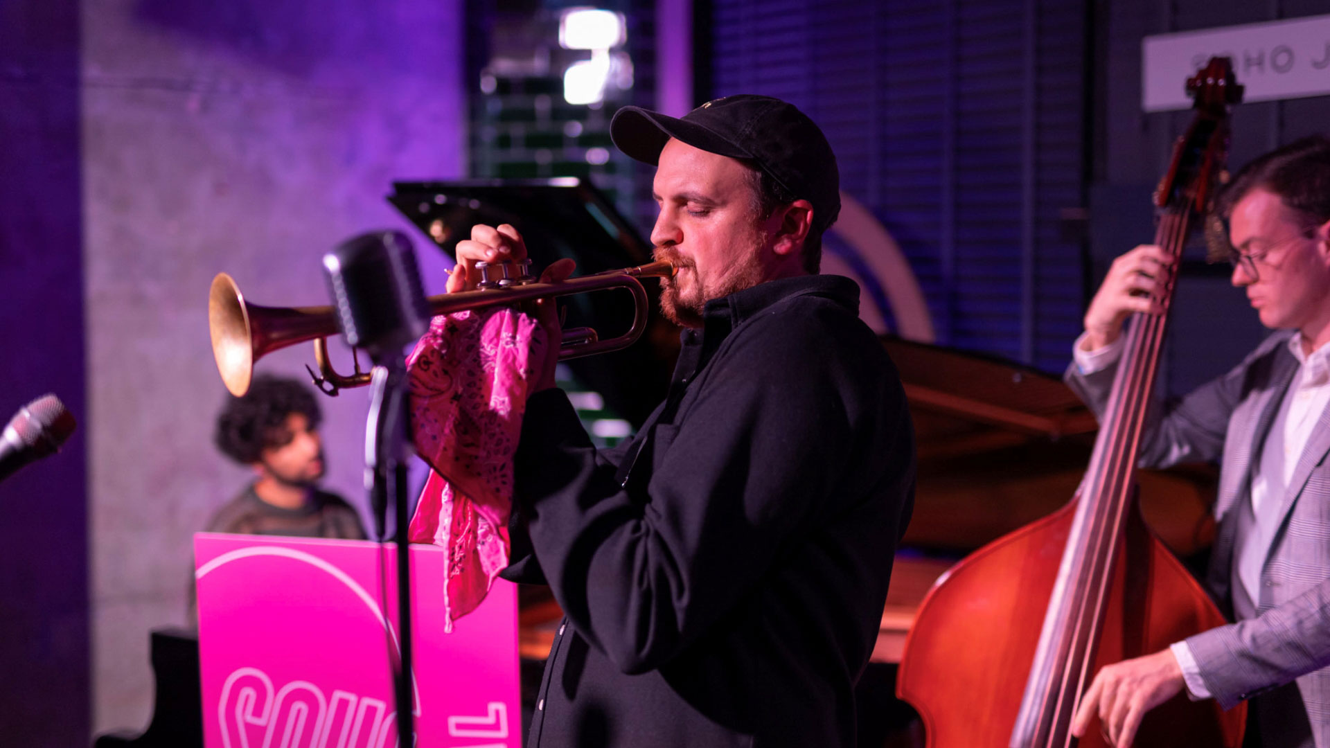 A man blowing into a trumpet onstage with other musicians during Soho Jazz Festival