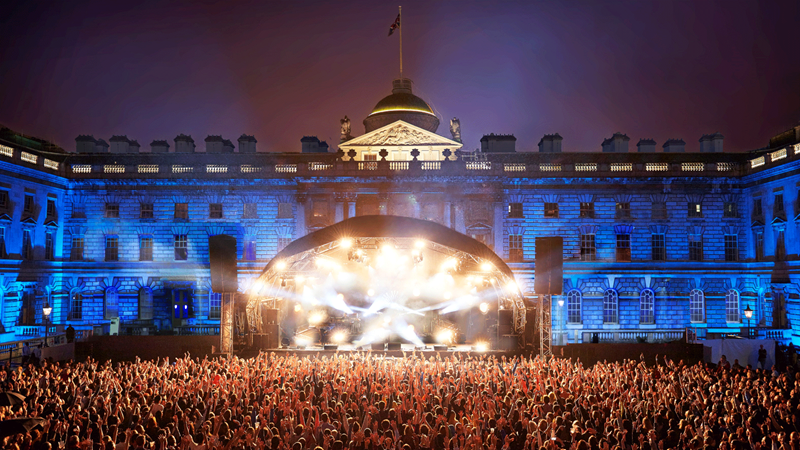 White lights illuminate the stage and blue lights light up Somerset House behind it with the crowd in the foreground