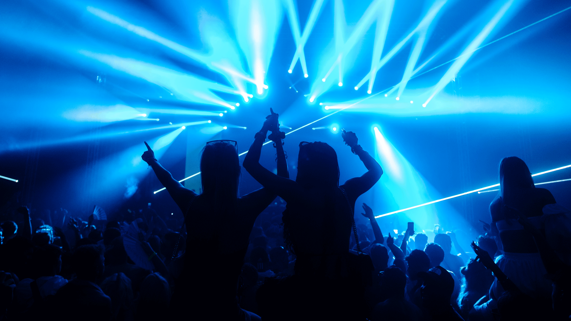 Silhouette of two friends on shoulders in the crowd in front of stage with glowing blue light lasers