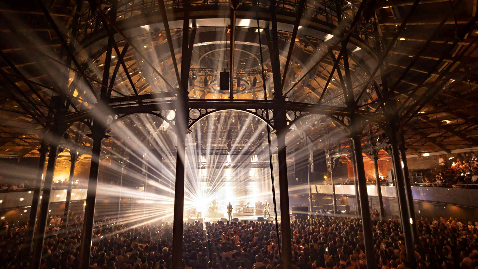 Bright lights shine through the architecture of Roundhouse as band play to a full crowd