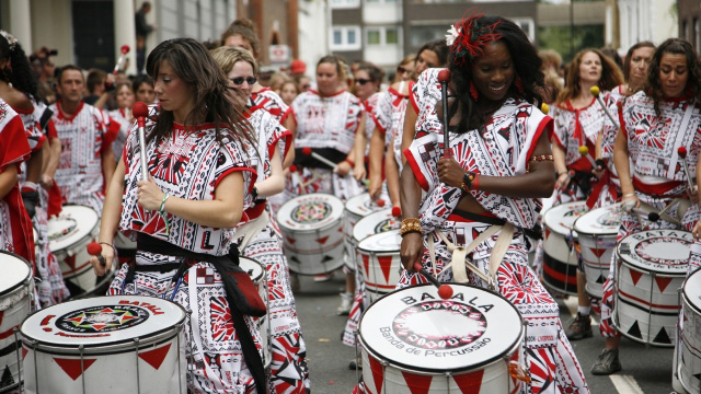 Notting Hill carnival performers dressed in authentic red and white clothing play the drums together