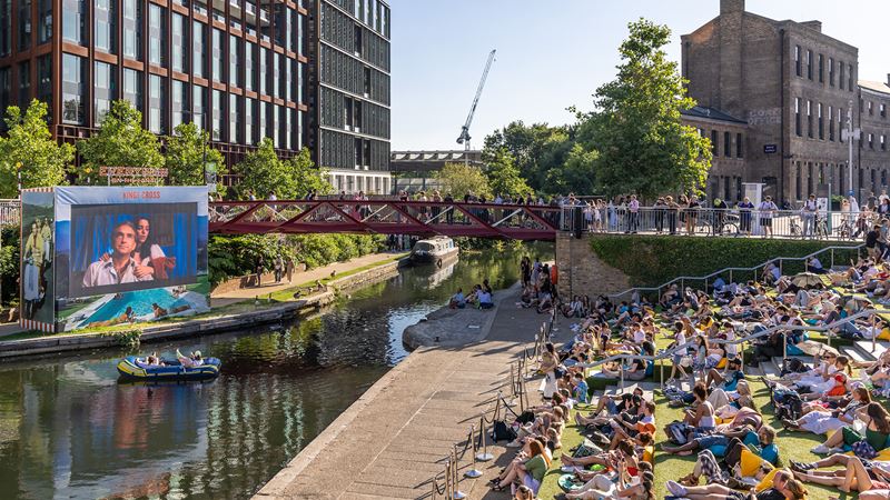 A screen on the canal with lots of viewers watching from across the canal.