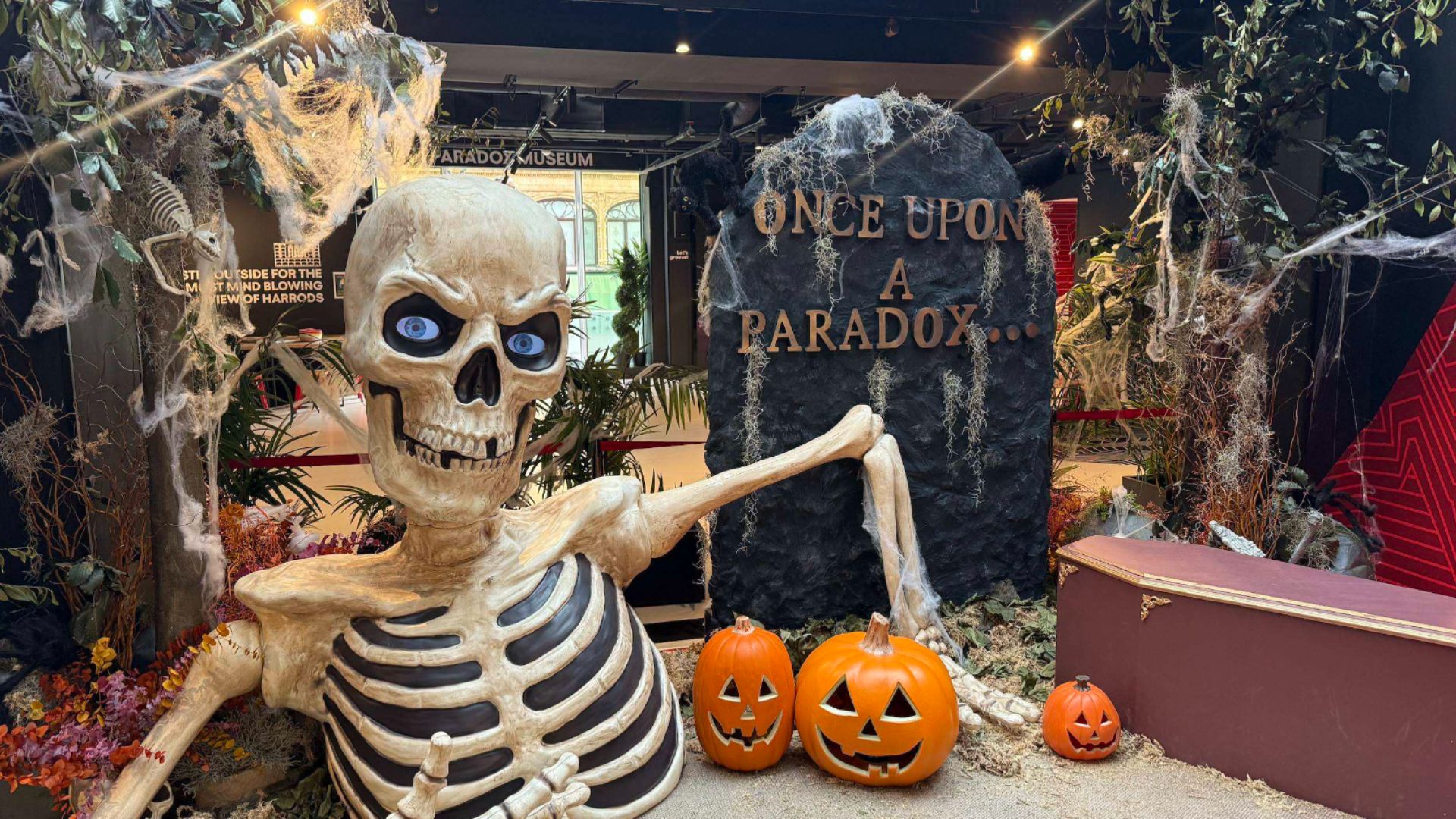 Follow a spooky Halloween trail through Paradox Museum London's immersive seasonal takeover. Image courtesy of Pink Neon Creative. Halloween display featuring a giant skeleton, pumpkins, cobwebs and a gravestone reading