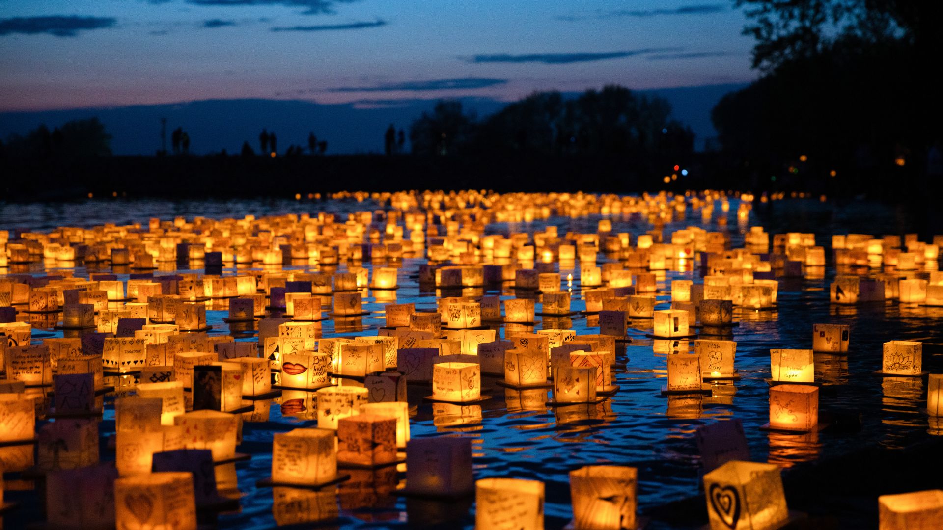 a low angle shot of a lake at dusk, filled with thousands of softly lit lanterns bobbing on top of the water