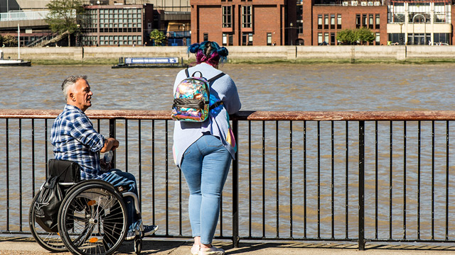 Many London attractions offer free wheelchairs to visitors. Image courtesy of Shutterstock. Man in a wheelchair talks to a woman on the South Bank in London