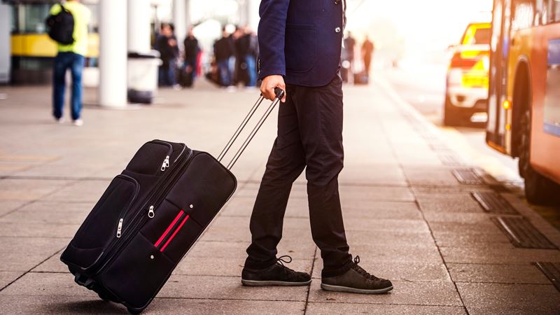 Person walking towards a bus with a suitcase.