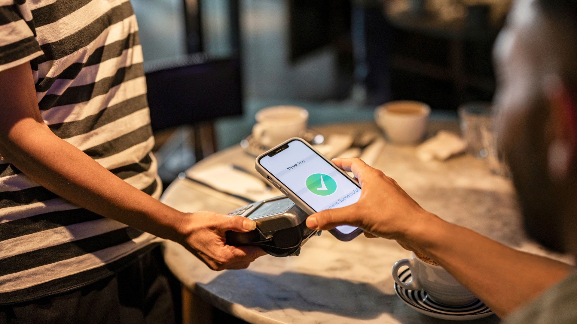 A photo of someone tapping their phone against a card reader to pay for service at a restaurant