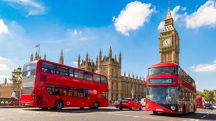 Two red double decker London buses drive past each other on opposite sides of Westminster Bridge with Big Ben and the Houses of Parliament in the background