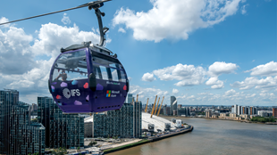 Une cabine du téléphérique londonien de couleur violette survole la Tamise donnant vue sur l'O2 et le sud de Londres.