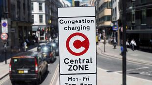 A congestion charge sign on a road with a black taxi behind on a sunny day