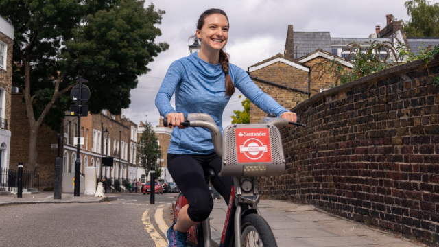 Eine Frau fährt ein Santander Cycle Leihfahrrad auf einer Straße in London