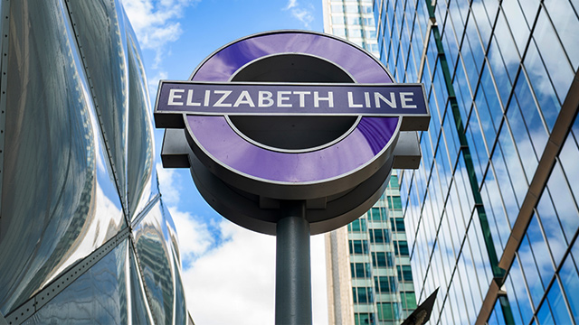 La ligne Elizabeth est le dernier ajout au vaste réseau de transport de Londres. Image reproduite avec l'aimable autorisation de Shutterstock. Panneau rond de la ligne Elizabeth devant des gratte-ciel à Londres par une journée ensoleillée.