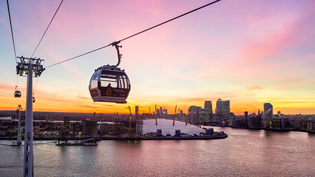 Eine der London Cable Cars ist weit über der Themse bei Sonnenuntergang zu sehen, mit dem The O2 im Hintergrund.