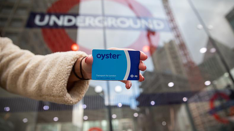 Hand of a woman holding an Oyster card outside the entrance of the underground