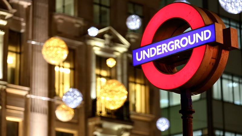 Ein beleuchtetes Schild der Londoner U-Bahn bei Nacht, mit Weihnachtsbeleuchtung im Hintergrund.
