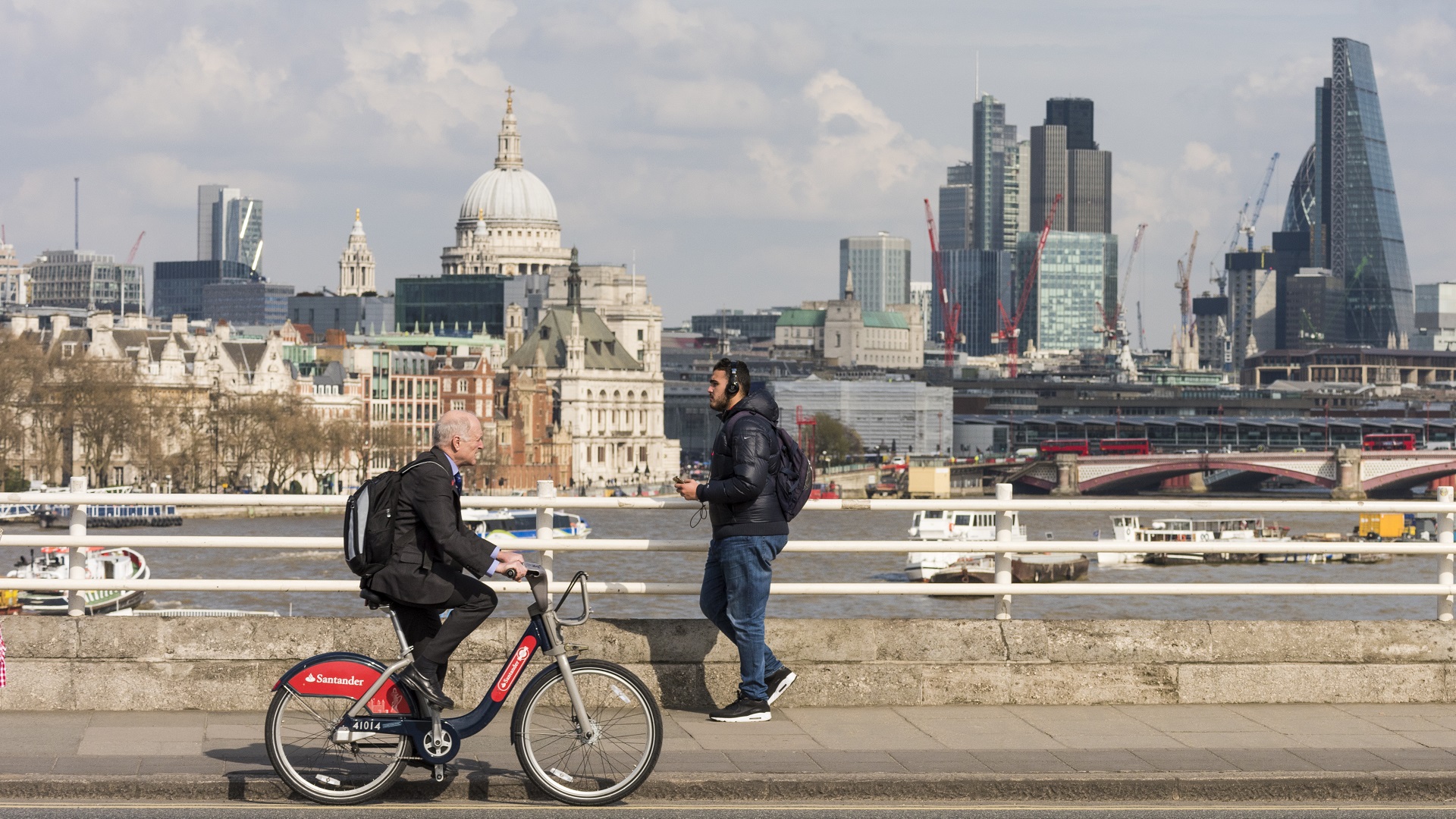 man cycling on bridge on a Santander Bike in front of London skyline