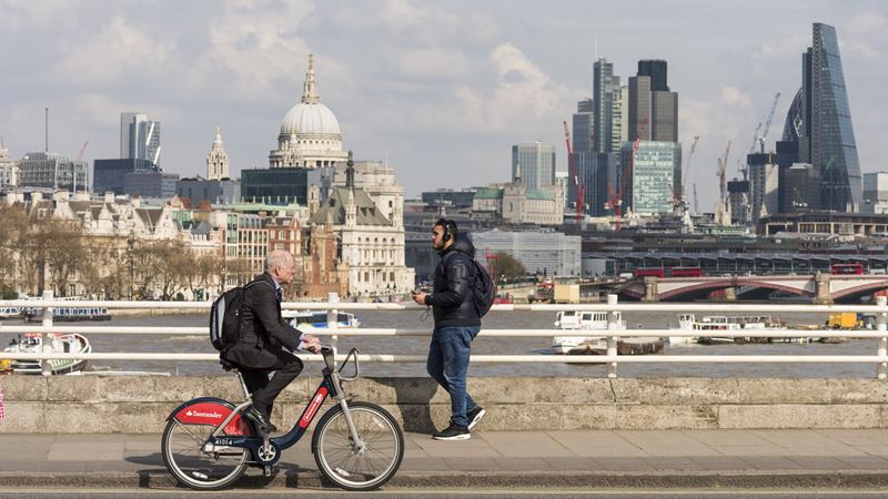 man cycling on bridge on a Santander Bike in front of London skyline