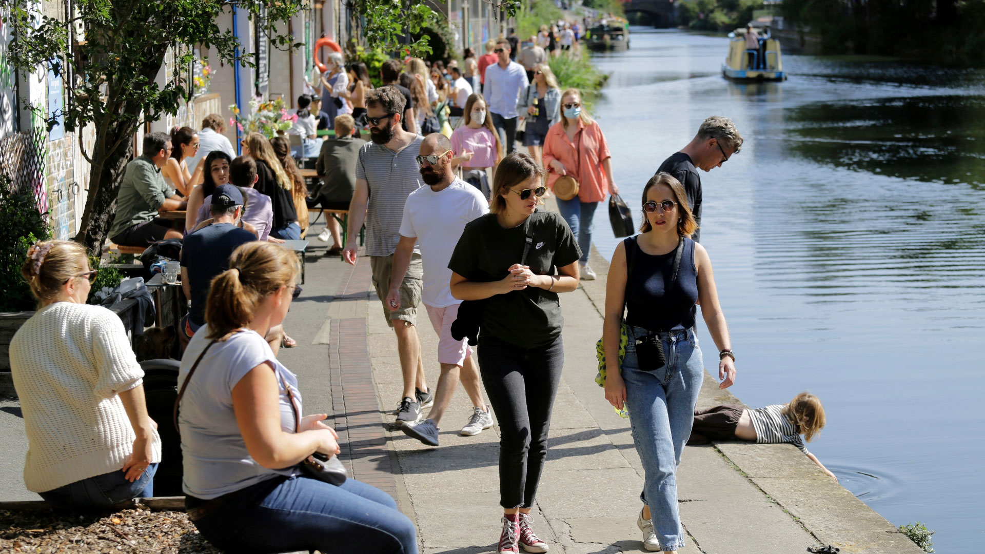 A photo of lots of people dressed for summer walking and sat along Regent's Canal as the sun shines down on them