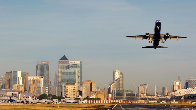 Ein Flugzeug hebt vom London City Airport ab mit den Wolkenkratzern von Canary Wharf im Hintergund