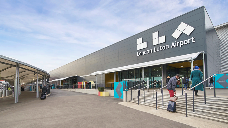 Entrance to London Luton Airport with passengers walking their suitcases up stairs
