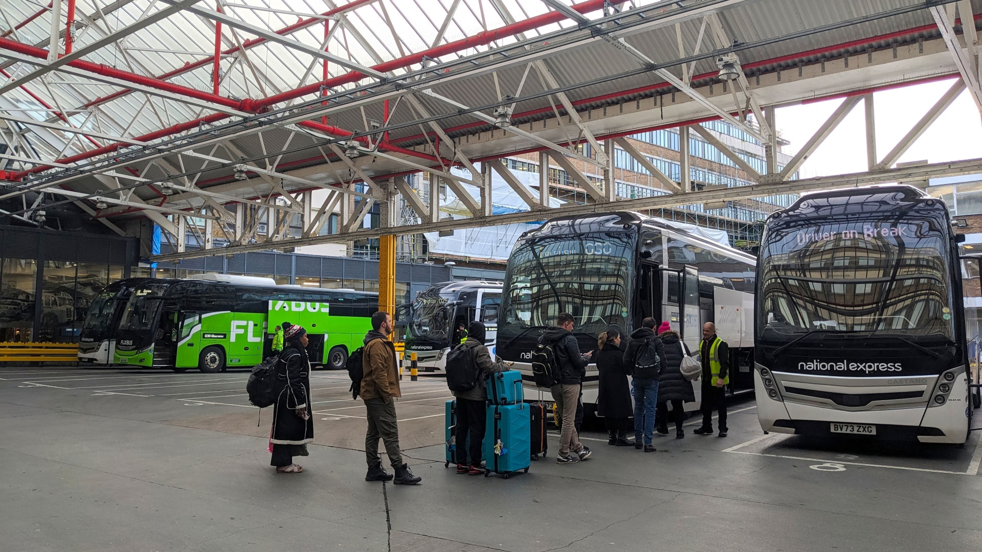 A photo of multiple people with luggage queuing to board a coach at a London coach station