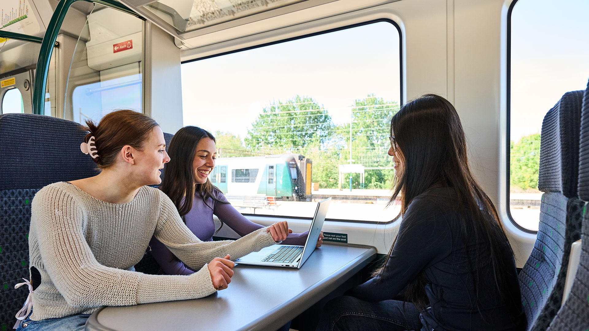 Plan a London trip by train with London Northwestern Railway. Image courtesy of London Northwestern Railway. Three girls sitting at a table on an LNR train with two looking at a laptop on a sunny day