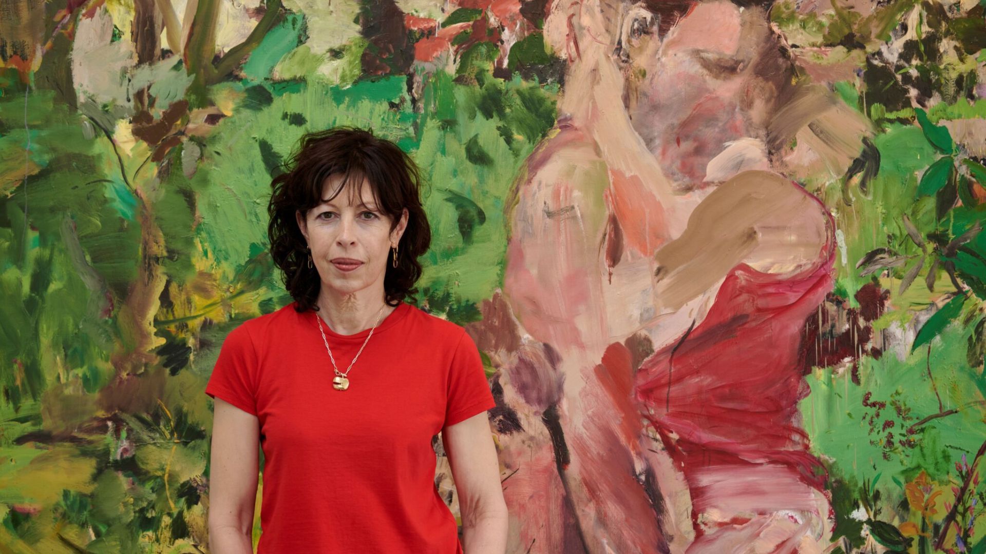 Artist Cecily Brown standing in front of abstract painting of two people kissing amongst nature.