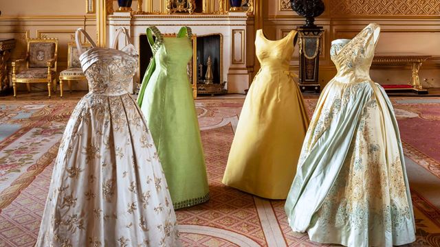 Four dresses worn by Queen Elizabeth II in the centre of a room at the King's Gallery.