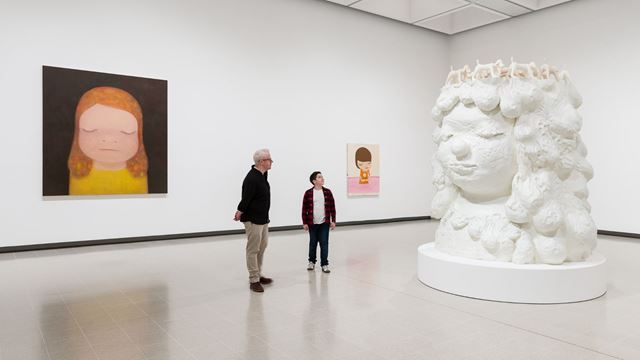Large sculpture of child-like figure head with paintings surrounding it.