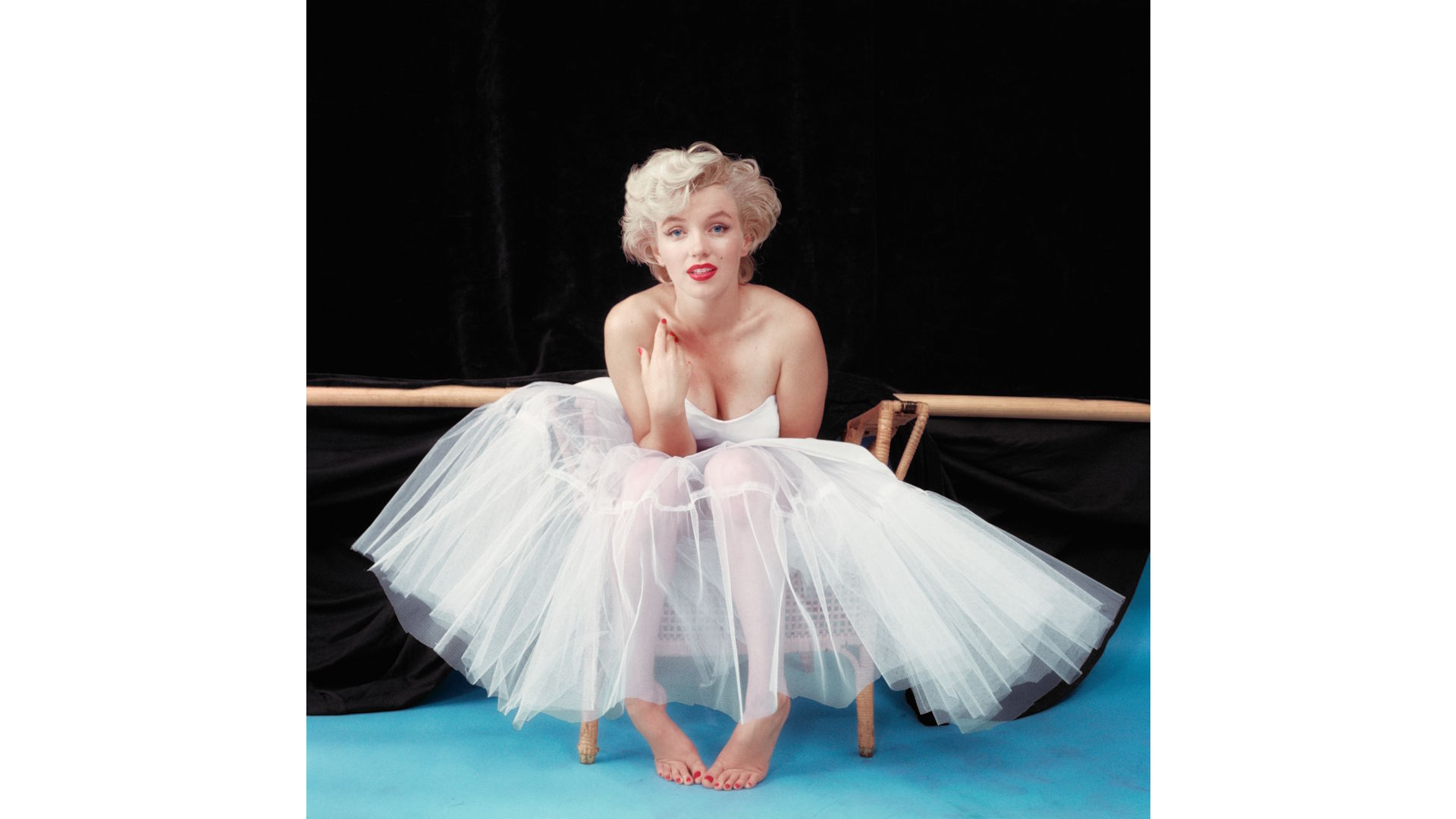 Marilyn Monroe, sitting down, wearing in a ballerina's dress with bare feet.
