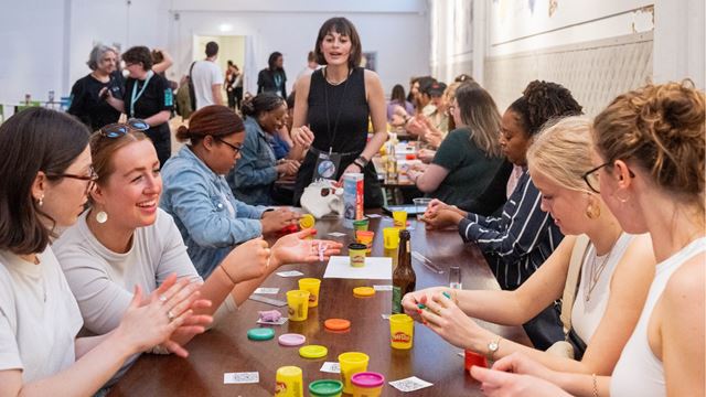Activity leader standing at head of table with group of people sitting down with Play-Doh in front of them.