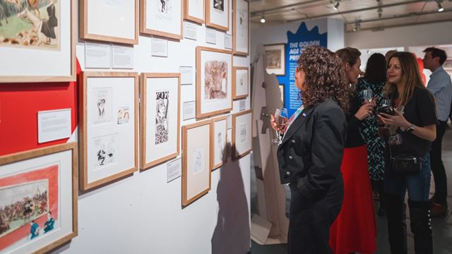 People gathered and looking up at artworks at The Cartoon Museum.