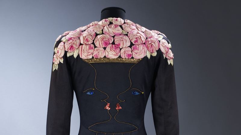 A couture jacket adorned with sculpted roses, on display at Schiaparelli: Fashion Becomes Art in London. Image courtesy of Victoria and Albert Museum, London. Ankle-length coat of black silk jersey with facial profiles forming a rose-filled vase, Elsa Schiaparelli, Jean Cocteau and Lesage, London, 1937 (c) Victoria and Albert Museum, London