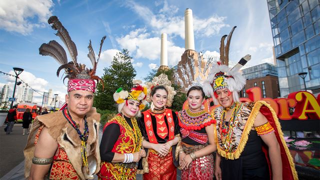 During the CelebrASIA festival, two men and three women wearing colourful, traditional ceremonial garments from South East Asian countries stand in front of Battersea Power Station.
