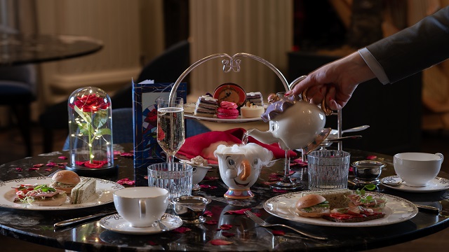 A beauty and the beast themed afternoon tea with sandwiches and cakes and film characters on a white table cloth.