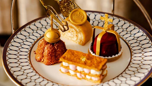a gold detailed plate with four royal-themed pastries with cream and decorative gold emblems