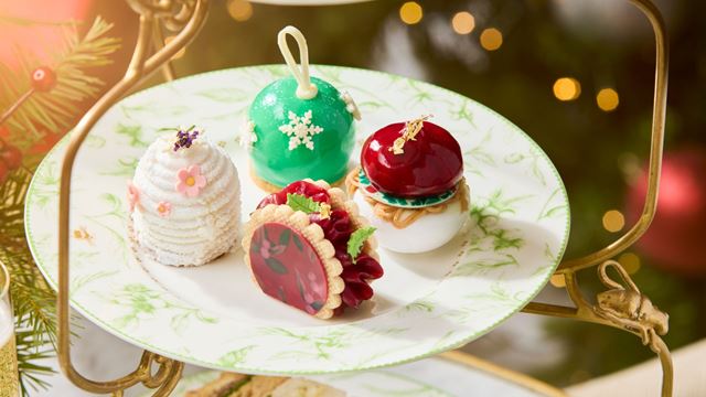 green and white detailed afternoon tea plate with four christmas-themed pastries and decorated with festive decorations in the background