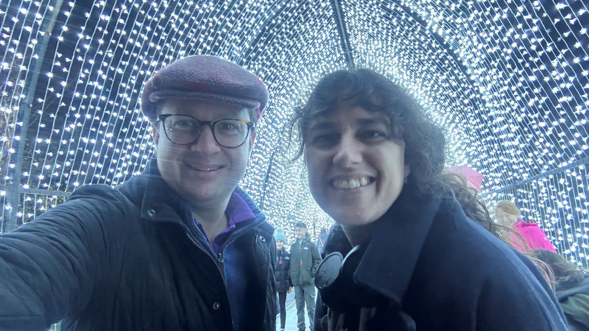 Take a selfie at the impressive Christmas Cathedral installation at Christmas at Kew. Photo credit: Jonny Payne © London & Partners. A man and woman pose for a selfie, at night, with a tunnel of white lights behind, during Christmas at Kew.