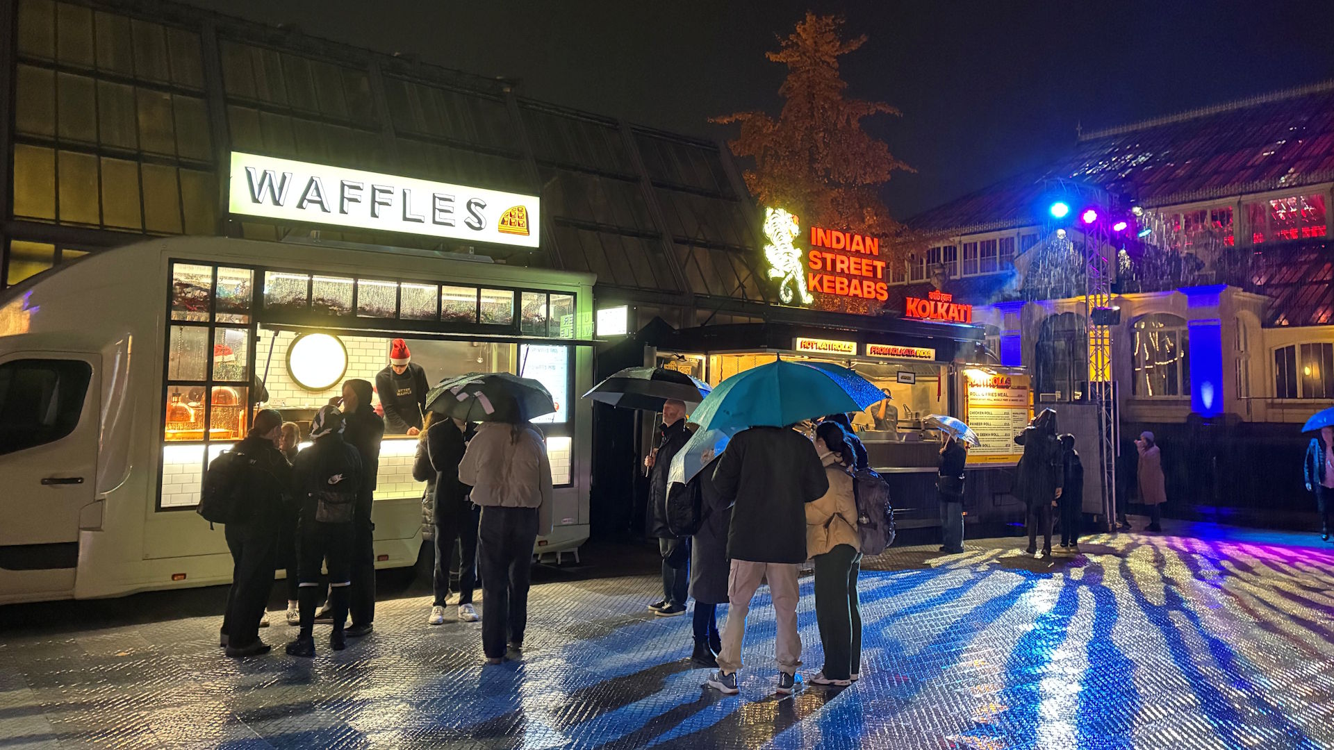 People gather outside two street food trucks, one showing Waffles and the other showing Indian Street Food signs at Christmas at Kew.