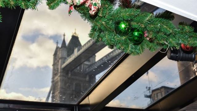 Christmas garland and baubles on a sightseeing boat, with Tower Bridge visible through the glass roof.