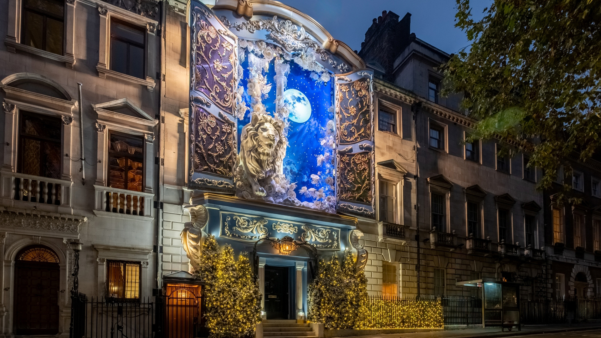 A close up photo of the Christmas facade on the front of Annabel's members club with wardrobe doors open to reveal a sky at night with the moon above and a giant lion, inspired by Narnia