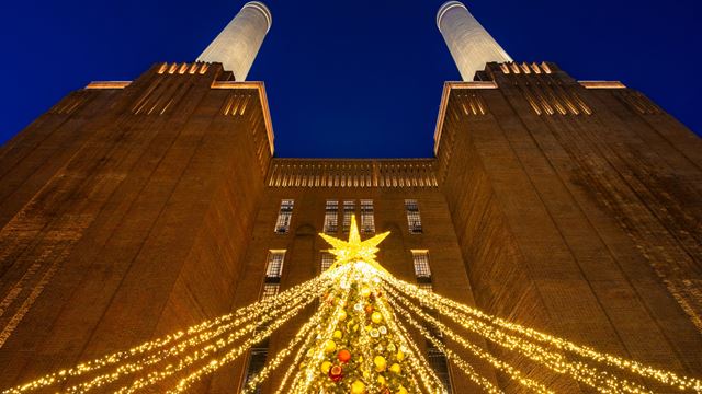 A photo of a Christmas tree in Malaysia Square with Battersea Power Station in the background and warm twinkling lights