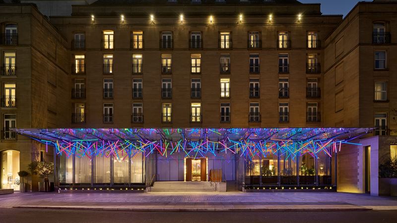See the festive light installation at The Berkeley as it moves with the flow of people. Credit: The Berkeley. Image courtesy of The Berkeley. A photo of the exterior of The Berkeley with its festive light installation hanging above the entrance, featuring neon beams in different colours