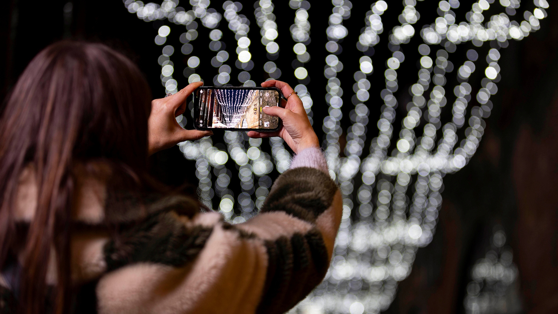 A photo of a woman taking a photo on her phone of a canopy of twinkling lights above Camden Market