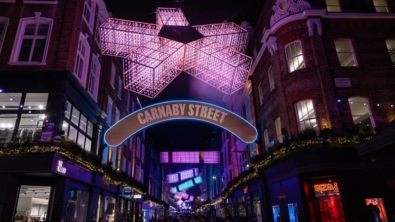 See the bright and bold Christmas lights illuminate Carnaby Street and surrounding areas for 2025. Credit: Carnaby Street. Image courtesy of W Communications. A photo of the 2025 Carnaby Christmas lights including abstract snowflake and cracker displays shining above the street in vibrant colours of orange, blue and pink